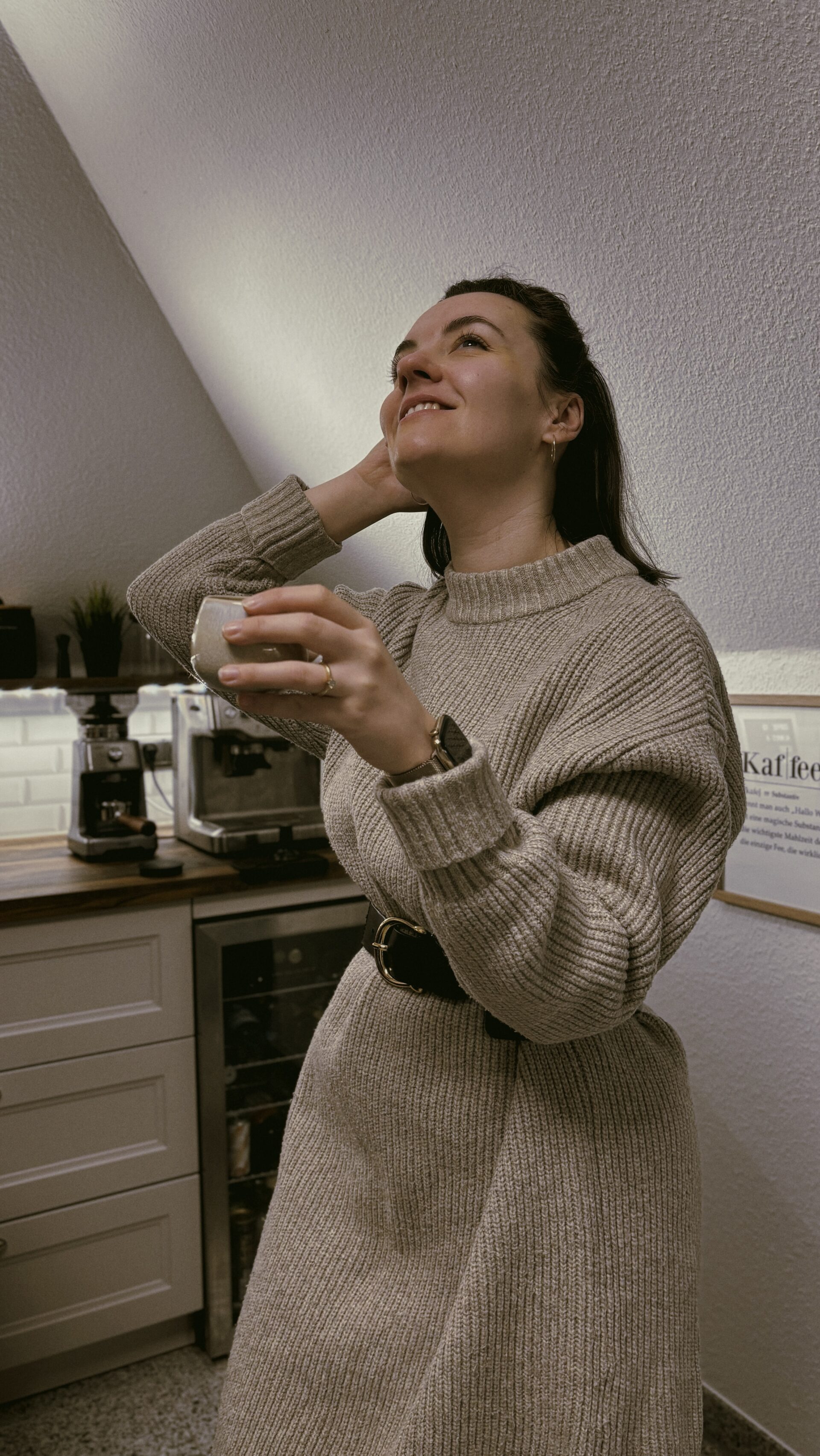 Frau in Strickkleid trinkt Kaffee in gemütlicher Küche