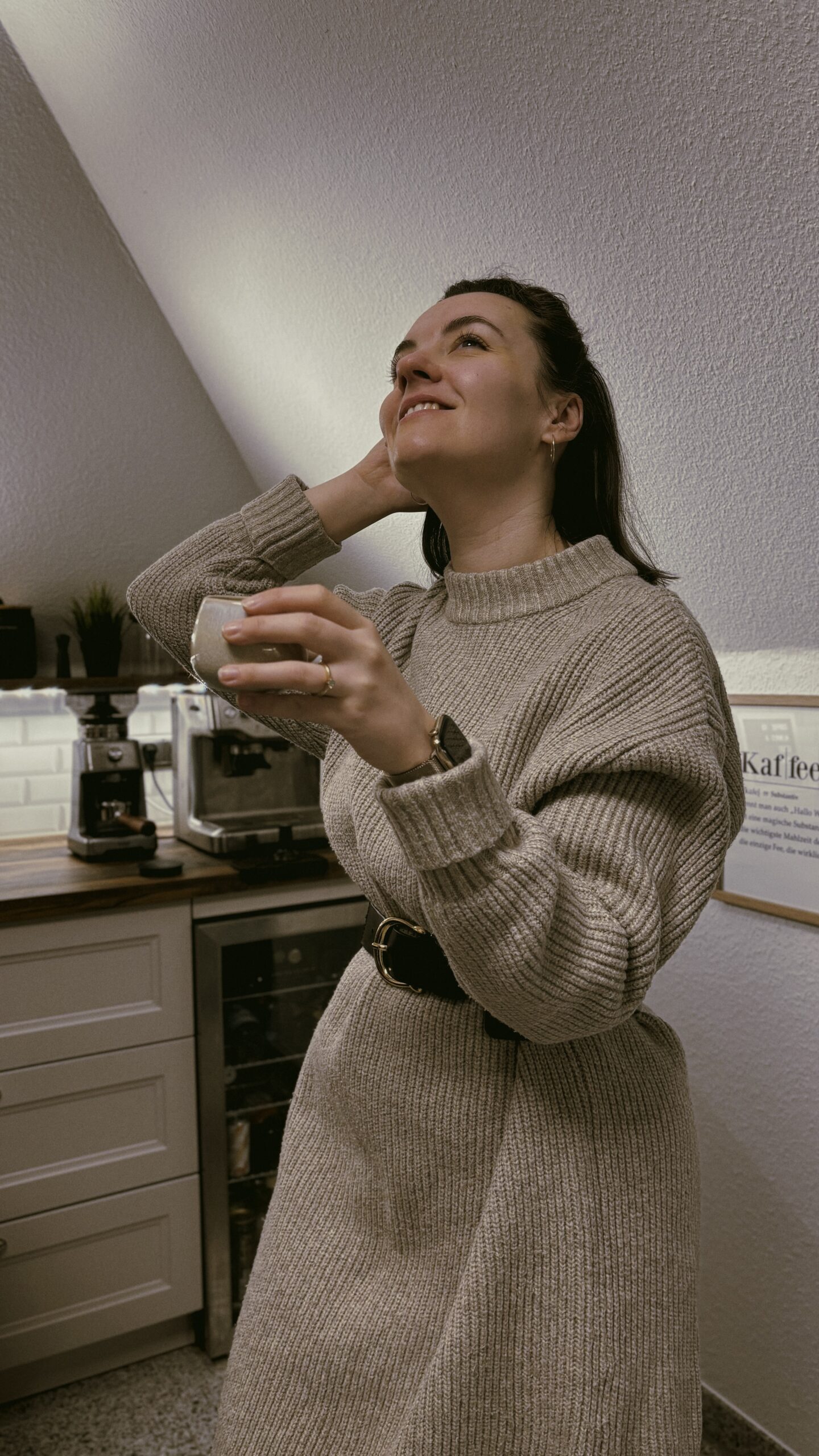 Frau in Strickkleid trinkt Kaffee in gemütlicher Küche