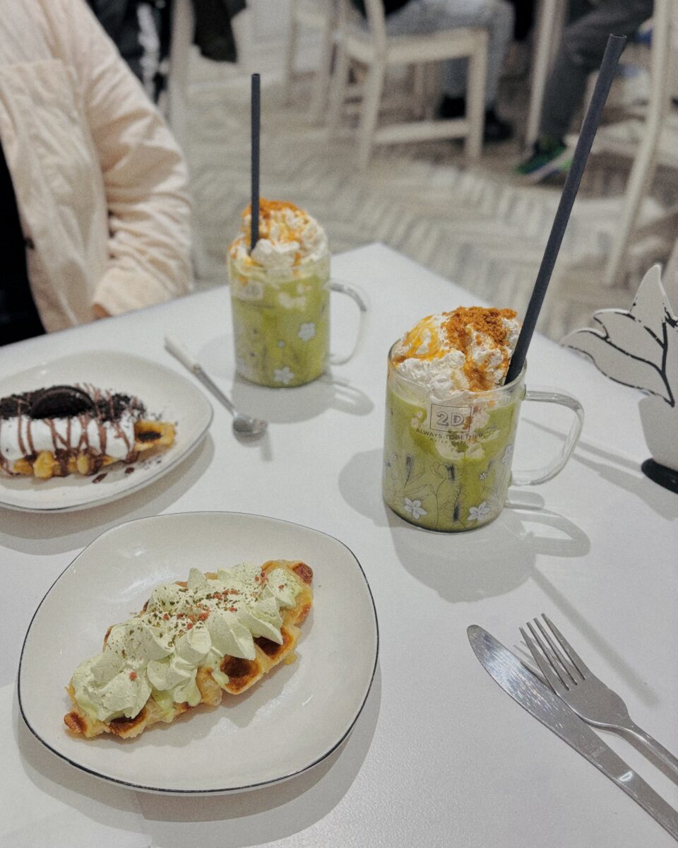 Zwei Gläser Matcha mit Sahne und knusprige Croffles im Café Always Together – ein farbenfroher Genussmoment im schwarz-weißen Interior.