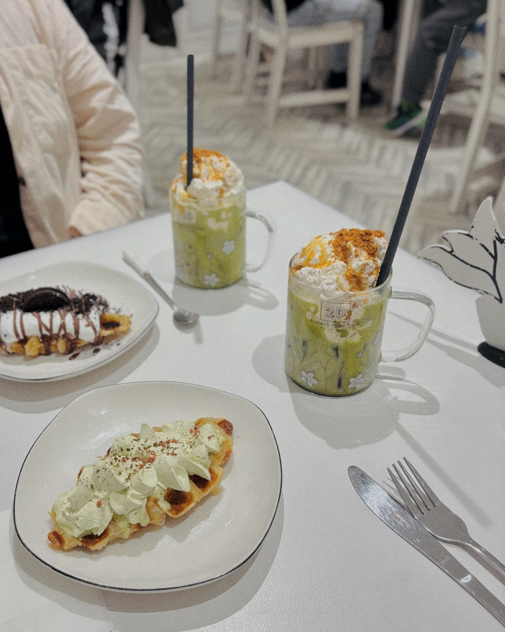 Zwei Gläser Matcha mit Sahne und knusprige Croffles im Café Always Together – ein farbenfroher Genussmoment im schwarz-weißen Interior.